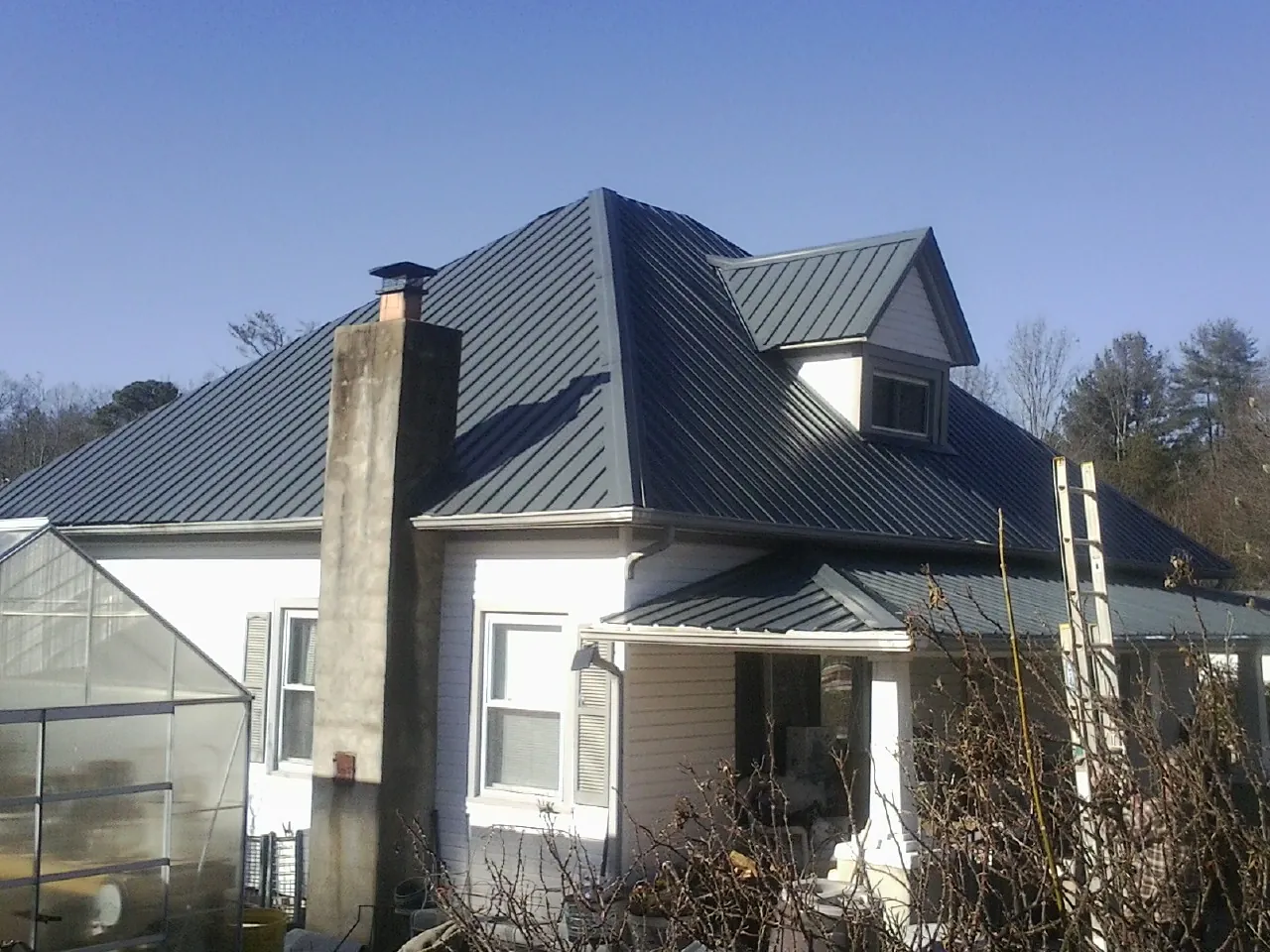 Dark blue standing seam metal roof on a white farmhouse with dormer — Slate & Tile Roof Repair by Roofing Brothers in Lilburn