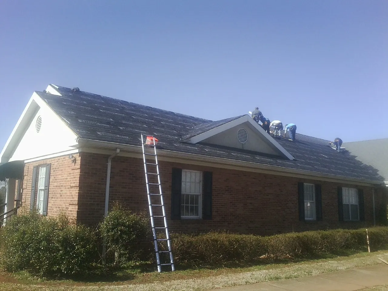 Crew tearing shingles off a brick ranch roof with a ladder set — Emergency Roof Repair work by our crew in Lilburn