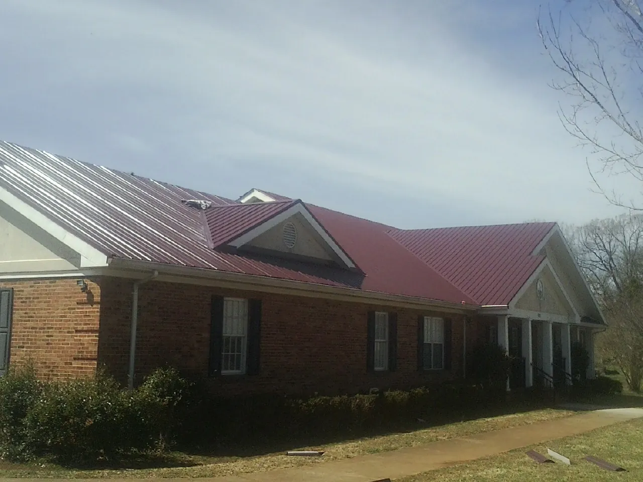 Red metal roof with gabled entries on a long brick building, from a Hail Damage Roof Repair job in Lilburn