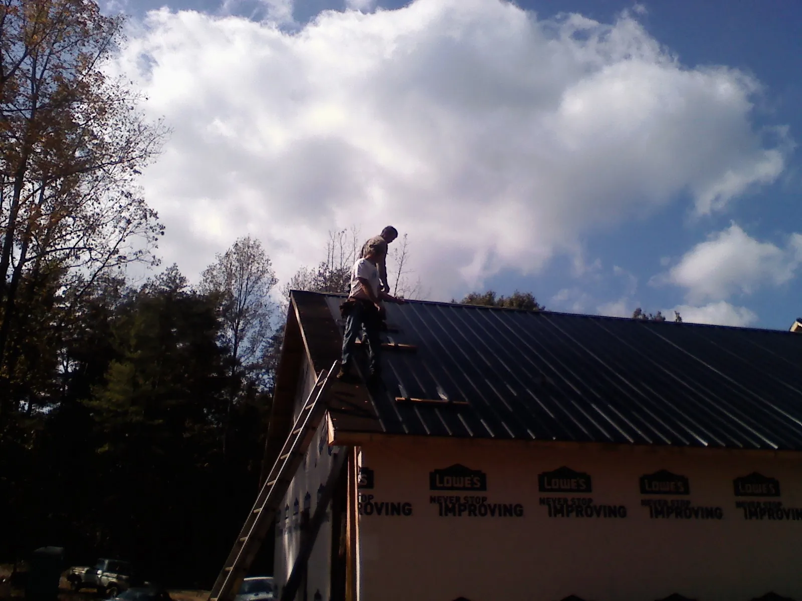 Roofer fastening dark metal panels high against a cloudy sky, from a Roof Inspection job in Lilburn